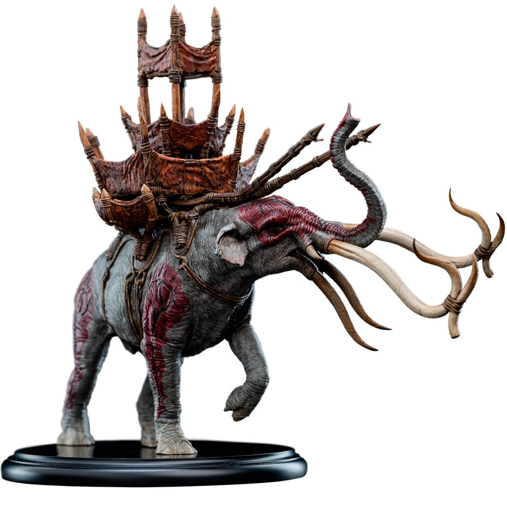 A detailed fantasy mammoth figurine with long tusks, carrying a large ornate crown-like structure on its back, standing on a round black base against a plain white background. LORD OF THE RINGS - Mumak in Battle 1:20 Statue (Weta Workshop)